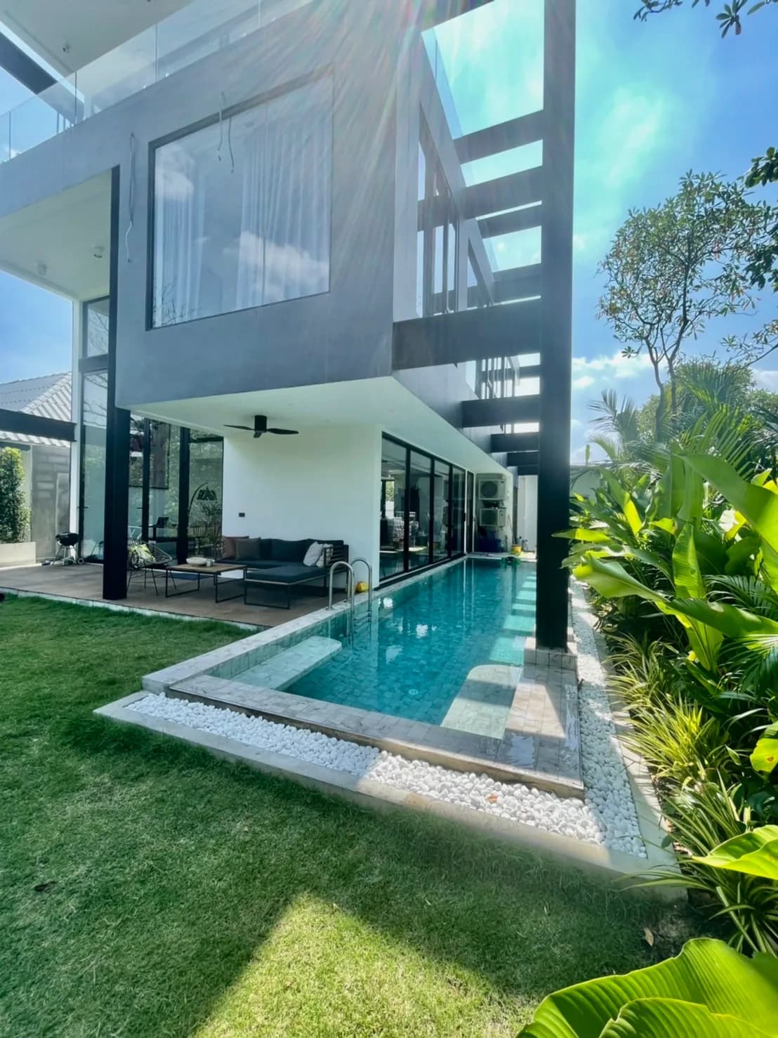 Two-storey black-steel exterior with private pool, framed by tropical garden