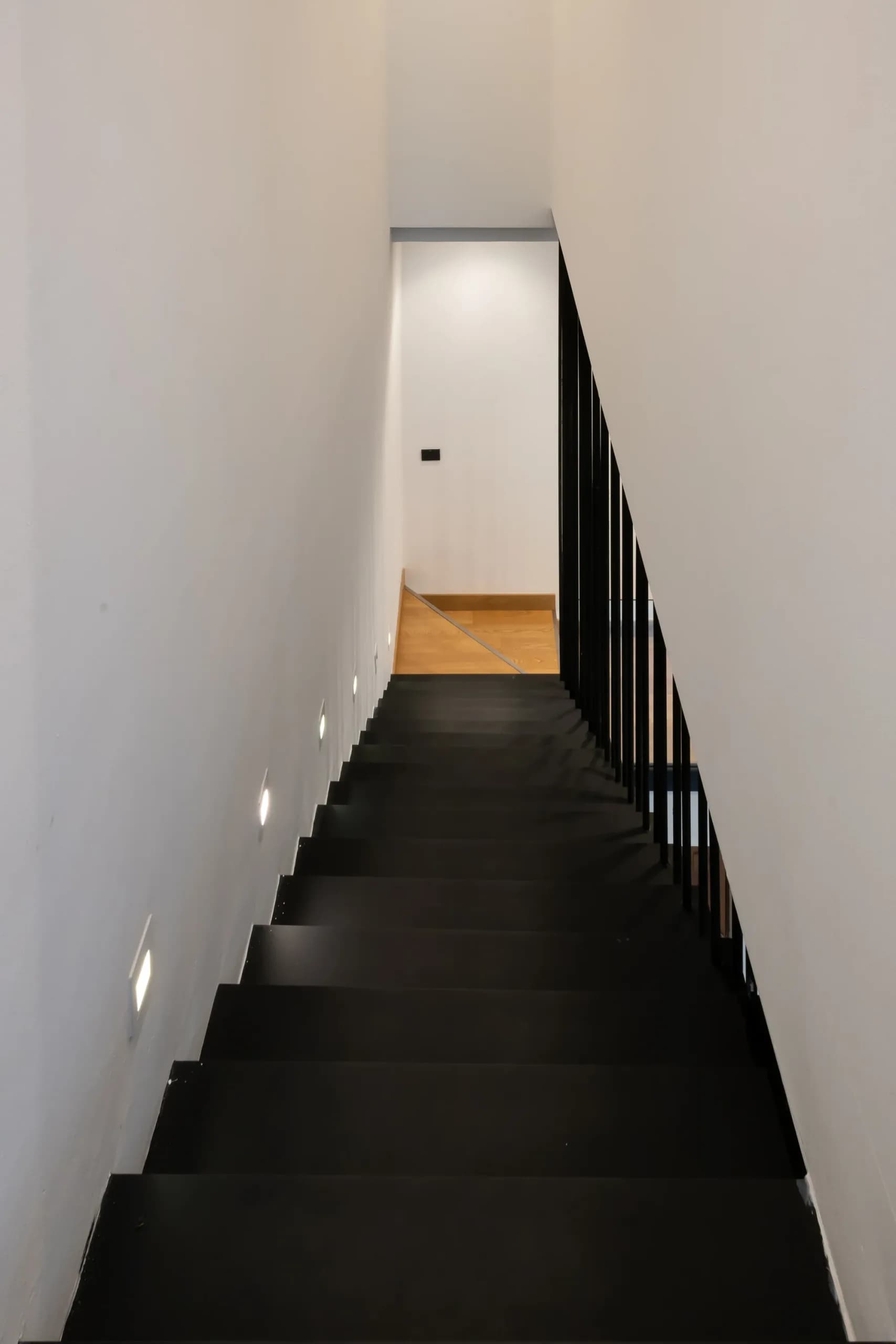 Black steel staircase rising between white walls